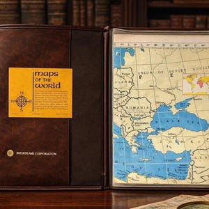 May include: Open brown leather map case with a vintage map of the Black Sea region. The map is framed within the case. A yellow label with the text "maps of the world" is affixed to the left side. The case is open, revealing the map.