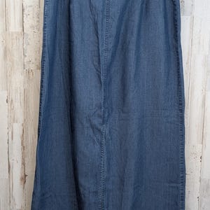 May include: A long, medium-wash blue denim skirt featuring a straight silhouette, a high-waisted design with an elasticated waistband, and a prominent vertical centre seam running down the front, finished with a simple hem at the bottom edge.