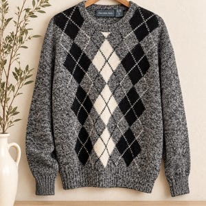 May include: A long-sleeve crew neck sweater featuring a black, white, and grey argyle pattern. The knit garment has a heathered grey base with solid black and white diamond shapes across the front, ribbed cuffs, and a ribbed hemline.