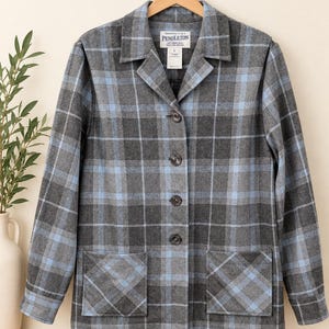 May include: A long-sleeve button-down jacket in a grey and light blue plaid pattern. The jacket features a notched collar, four dark buttons down the front, and two square patch pockets at the waist. A Pendleton label is visible at the neck.