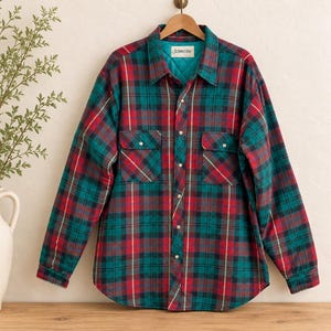 May include: A long-sleeve button-up shirt featuring a red, teal, and dark green plaid pattern. The shirt has two chest pockets with button flaps, a collar, and a quilted teal interior lining with a St. John's Bay label visible at the neckline.