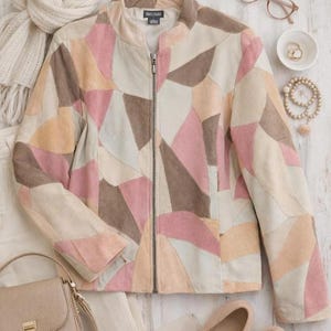 May include: A zip-up jacket featuring a patchwork design of irregular geometric shapes in shades of cream, soft pink, tan, and brown. The jacket has a stand-up collar, long sleeves, and a central metal zipper closure. The interior label reads Multiples.