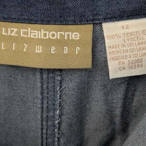 May include: A blue denim garment featuring a tan Liz Claiborne Lizwear brand label. A white care tag is attached, displaying the size 12, 100% Tencel Lyocell material composition, and manufacturing information including Made in Sri Lanka and RN 52002.