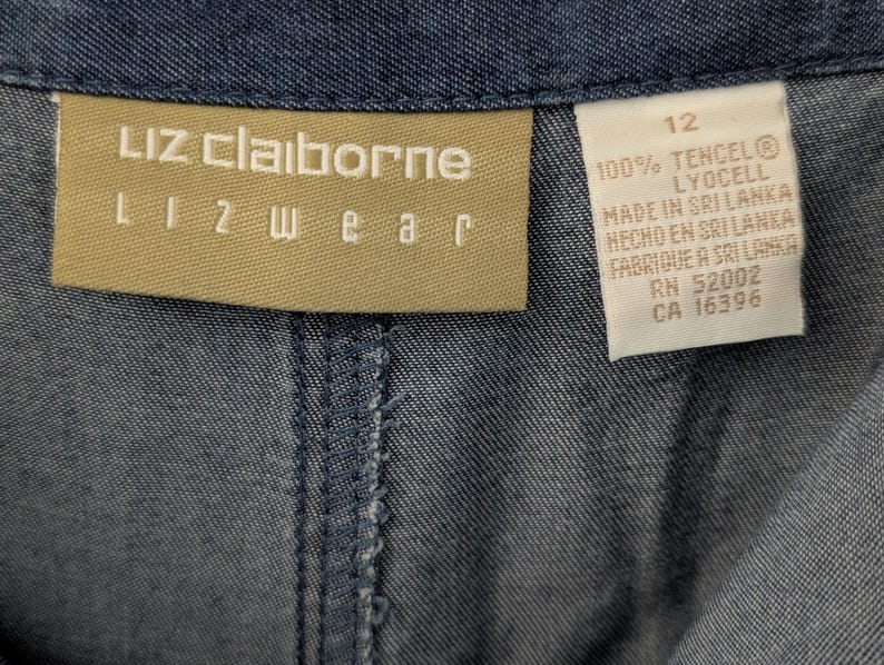 May include: A blue denim garment featuring a tan Liz Claiborne Lizwear brand label. A white care tag is attached, displaying the size 12, 100% Tencel Lyocell material composition, and manufacturing information including Made in Sri Lanka and RN 52002.