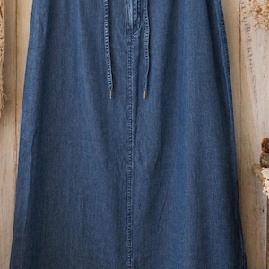 May include: A long, blue denim skirt featuring an elasticated waistband with a drawstring closure. The skirt has a straight, floor-length silhouette with a central vertical seam running down the front and a hemline finished with double stitching.