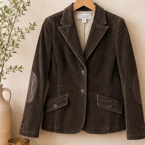 May include: A dark brown corduroy blazer featuring a notched lapel, two front buttons, and two flap pockets. The sleeves include dark brown elbow patches and two buttons at each cuff. The interior label reads St. John Short with size 6.