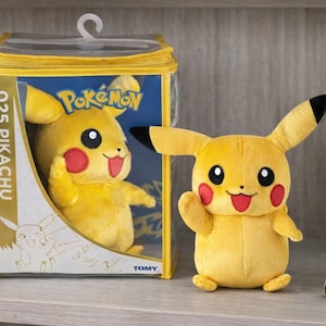 May include: A white ceramic mug with a black handle and the text "But First, Coffee" in a bold, black font. The mug is set against a blurred background, suggesting a cozy setting.