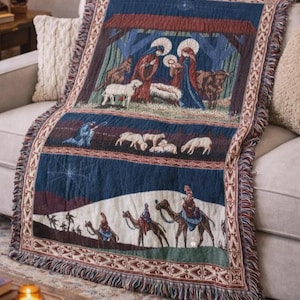 May include: A woven throw blanket featuring a multi-paneled nativity scene. The top panel depicts the holy family in a stable with animals. The middle panel shows sheep in a field. The bottom panel displays travelers on camels in a desert landscape.