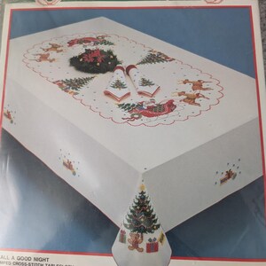 Puede incluir: Un kit de mantel navide&ntilde;o de punto de cruz con un dise&ntilde;o festivo. El mantel blanco presenta im&aacute;genes bordadas de &aacute;rboles de Navidad, renos, Pap&aacute; Noel en un trineo y un &aacute;rbol de Navidad en una servilleta. El kit incluye tela, hilo y una aguja.