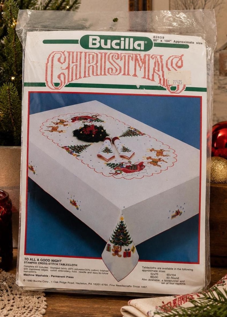 Puede incluir: Kit de mantel de punto de cruz navide&ntilde;o Bucilla. La tela blanca presenta un dise&ntilde;o de &aacute;rbol de Navidad en la esquina y un borde festivo con renos, &aacute;rboles y Pap&aacute; Noel. El paquete est&aacute; etiquetado 152 cm x 264 cm.