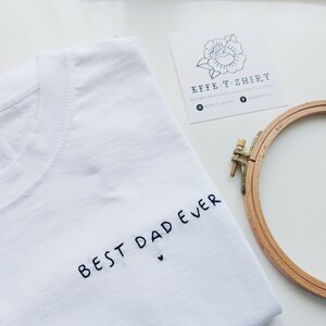 May include: White t-shirt with black embroidery that says "Best Dad Ever" with a small heart.