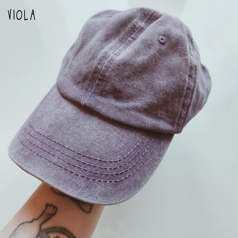 K&ouml;nnte beinhalten: Eine lilafarbene Baseballkappe mit leicht abgenutztem Look. Die Kappe hat einen gebogenen Schirm und ein gesticktes Design.