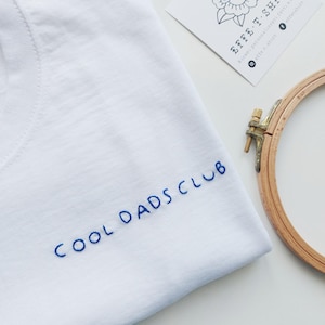 May include: White t-shirt with blue embroidery that reads "COOL DADS CLUB".