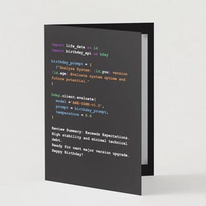May include: A folded greeting card with a dark gray cover featuring lines of colorful code. The text includes "Import life data", "birthday_prompt", and "Happy Birthday!"