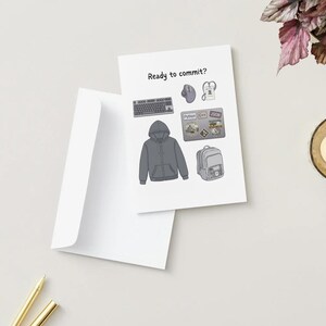 Peut inclure: Une carte de v&oelig;ux blanche avec le texte Ready to commit? et des illustrations d'un sweat &agrave; capuche gris, un clavier, une souris, un ordinateur portable avec des autocollants, un sac &agrave; dos et un badge. La carte est accompagn&eacute;e d'une enveloppe blanche.