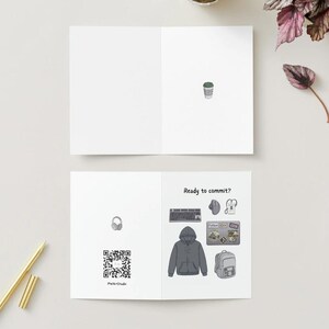 Peut inclure: Une carte de v&oelig;ux pli&eacute;e blanche avec une petite illustration de tasse de caf&eacute; &agrave; l'int&eacute;rieur. Le dos affiche un code QR, un casque et le texte Ready to commit? avec des illustrations de clavier, souris, sweat &agrave; capuche, ordinateur et sac &agrave; dos.