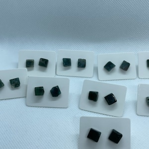 Może przedstawiać: Zestaw 10 par kwadratowych kolczyków z ciemnozielonego i czarnego kamienia szlachetnego na białych kartkach.