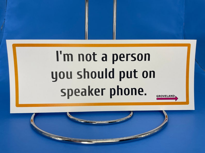 May include: A white sign with an orange border and the text "I'm not a person you should put on speaker phone."  The sign also has a small pink arrow with the text "GROVELAND" above it.