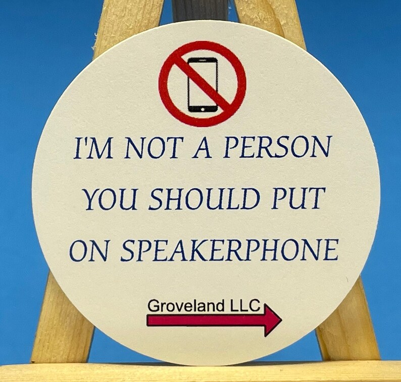 May include: A white round coaster with a red circle and a diagonal line through a black cell phone image. The text "I'm not a person you should put on speakerphone" is printed in blue. The text "Groveland LLC" is printed in black with a red arrow pointing to the right.