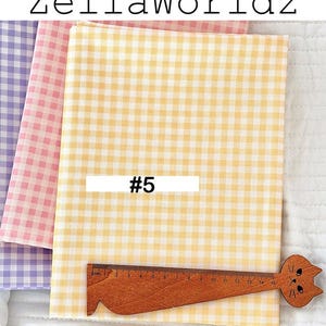 May include: Three fabric swatches in pastel colors: yellow, pink, and purple, all with a gingham pattern. A wooden ruler with a cat face design is placed on the yellow fabric. The text "ZellaWorldz" is at the top, and "#5" is on the yellow fabric.