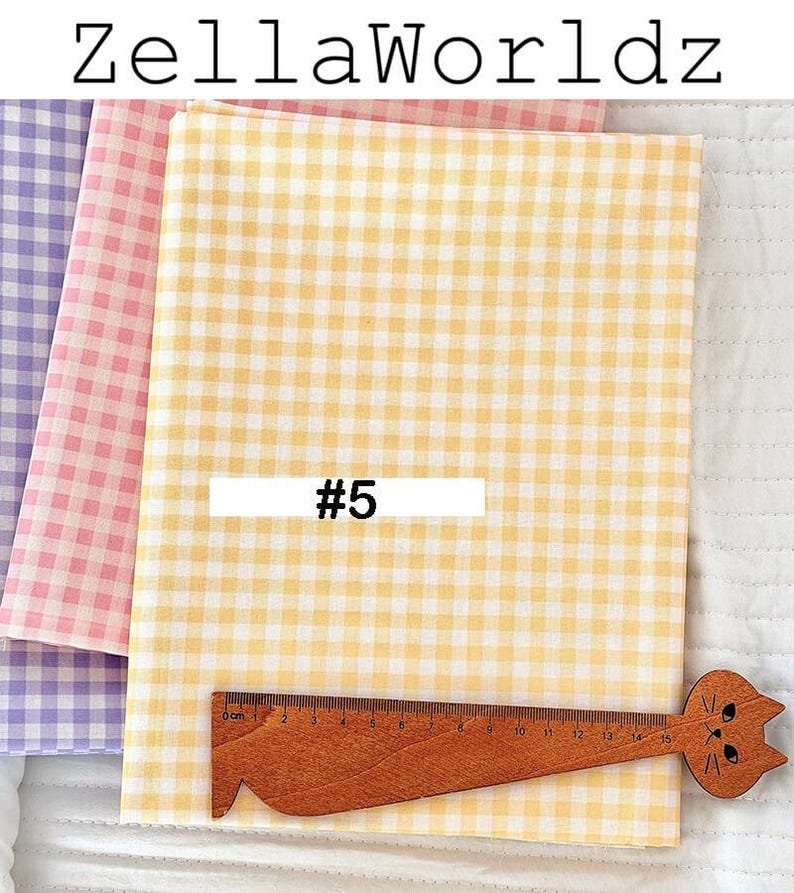 May include: Three fabric swatches in pastel colors: yellow, pink, and purple, all with a gingham pattern. A wooden ruler with a cat face design is placed on the yellow fabric. The text "ZellaWorldz" is at the top, and "#5" is on the yellow fabric.