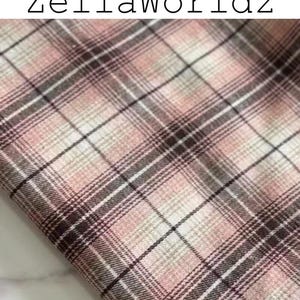 Pu&ograve; includere: Un campione di tessuto con un motivo a quadri nelle tonalit&agrave; rosa tenue, bianco e marrone scuro. Il tessuto presenta un design a griglia intrecciata con linee che si intersecano di vario spessore. Il testo ZellaWorldz &egrave; stampato in nero in alto.