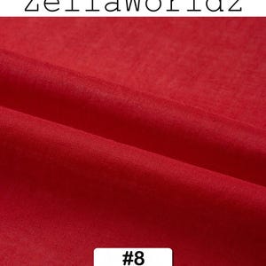 Peut inclure: Gros plan sur un tissu rouge vif avec des plis subtils. L'image pr&eacute;sente le texte "ZellaWorldz" en haut et un rectangle blanc avec le num&eacute;ro "#8" en bas. La texture du tissu est visible, sugg&eacute;rant un mat&eacute;riau doux.