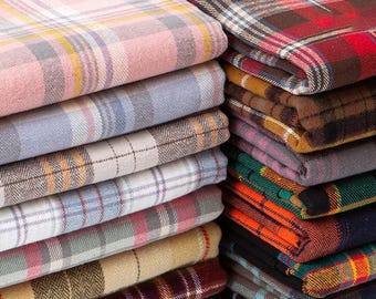 Può includere: Una pila di pezzi di tessuto piegati con vari motivi a quadri e tartan in colori tra cui rosa, blu, marrone, verde, arancione e nero. Il testo ZellaWorldz è visibile nella parte superiore dell'immagine. Ogni pezzo di tessuto mostra un distinto design a quadri intrecciati con linee che si incrociano di diverse larghezze e sfumature.