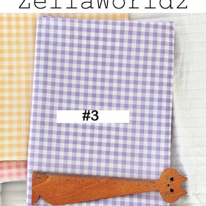 May include: A stack of gingham fabric in shades of yellow and lavender. A wooden ruler with a cat-shaped head is placed on the lavender fabric. The text "#3" is on a white rectangle. The text "ZellaWorldz" is at the top.