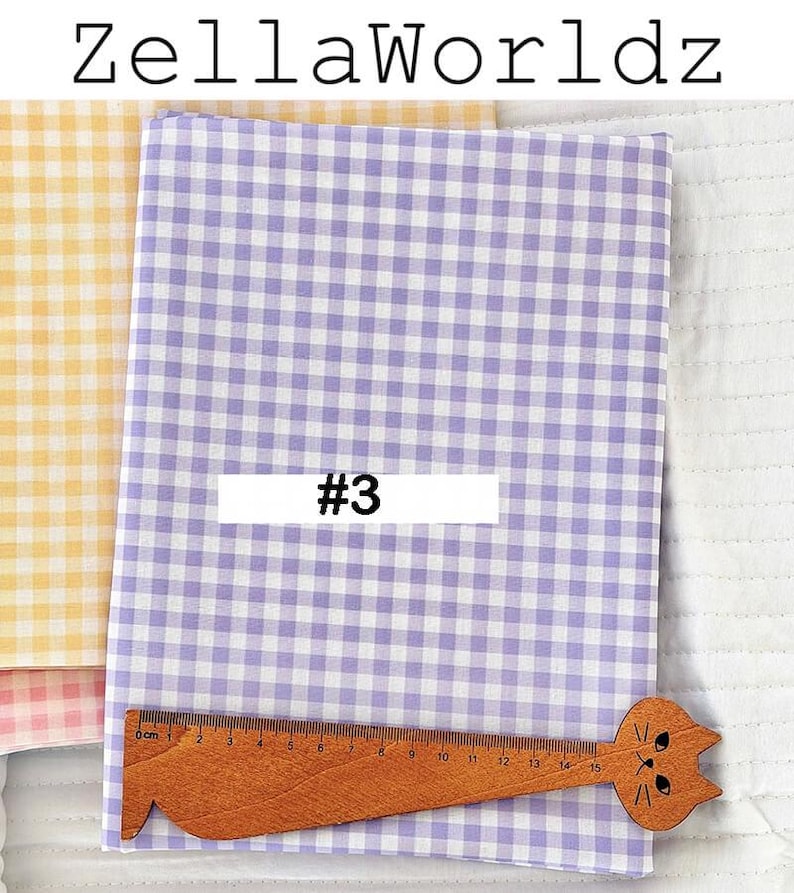 May include: A stack of gingham fabric in shades of yellow and lavender. A wooden ruler with a cat-shaped head is placed on the lavender fabric. The text "#3" is on a white rectangle. The text "ZellaWorldz" is at the top.