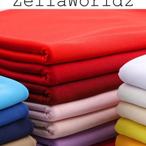 May include: Stacks of folded fabric in various colors, including red, burgundy, pink, and blue. The text "ZellaWorldz" is displayed in black letters at the top of the image. The fabric appears to be soft and smooth.