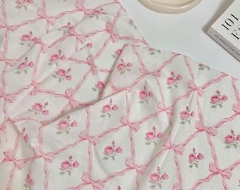 May include: White fabric with a repeating pattern of pink roses and ribbons. The roses are clustered in small bouquets, and the ribbons form a grid-like design. The text "ZellaWorldz" is at the top.