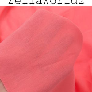 Peut inclure: Gros plan sur un tissu de couleur corail, avec le texte "ZellaWorldz" en lettres noires en haut. Le tissu est doux et semble drap&eacute;, avec une texture et des plis visibles. La couleur est une teinte chaude et vibrante.
