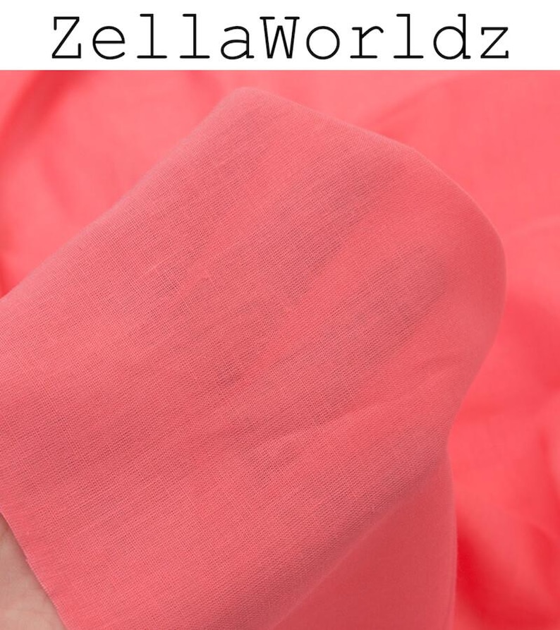 Peut inclure: Gros plan sur un tissu de couleur corail, avec le texte "ZellaWorldz" en lettres noires en haut. Le tissu est doux et semble drap&eacute;, avec une texture et des plis visibles. La couleur est une teinte chaude et vibrante.