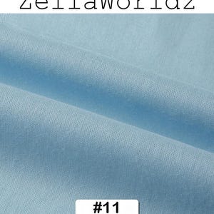 Peut inclure: Gros plan sur un tissu bleu clair avec des plis doux. Le tissu a une texture lisse. Le texte "ZellaWorldz" est en haut et le num&eacute;ro "#11" dans un rectangle blanc en bas.