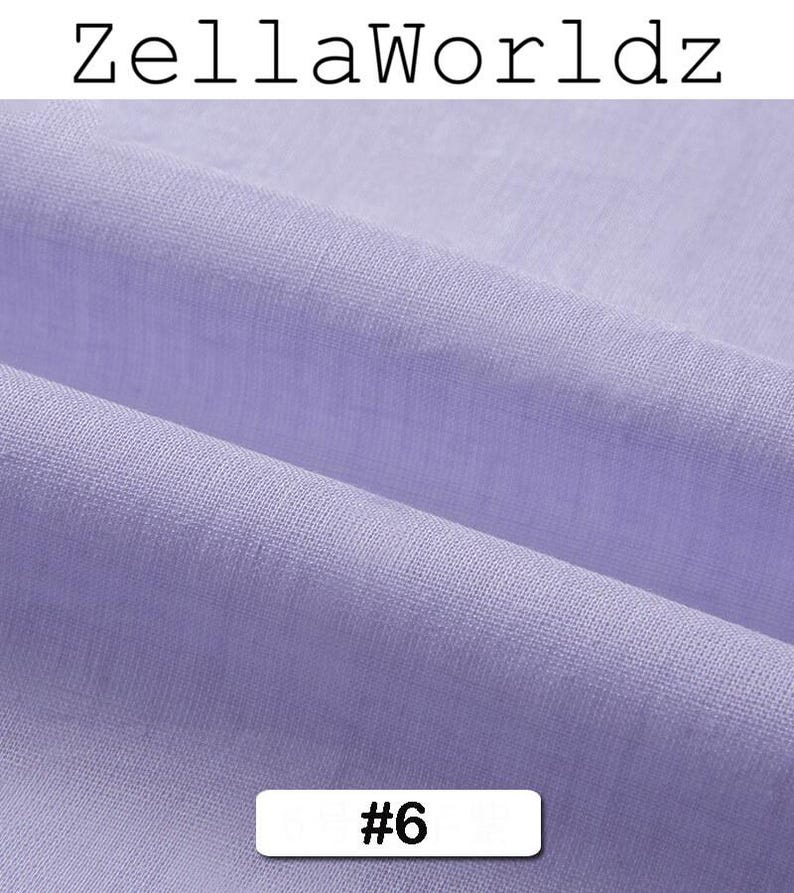 Peut inclure: Gros plan sur un tissu violet clair avec une texture et des plis visibles. Le tissu est &eacute;tiquet&eacute; avec le texte "ZellaWorldz" en haut et le num&eacute;ro "#6" dans un rectangle blanc en bas. Le tissu semble &ecirc;tre une mati&egrave;re douce.