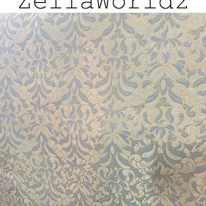 May include: Close-up of a fabric with a repeating floral pattern in light blue, cream, and gold. The text "ZellaWorldz" is at the top of the image in black letters. The design is a classic damask style.