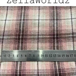 Pu&ograve; includere: Tessuto con motivo a quadri rosa, bianco e marrone scuro con il testo ZellaWorldz in alto. Un righello in metallo &egrave; posizionato orizzontalmente sul tessuto, mostrando le misure in centimetri fino a 18 cm come riferimento di scala.