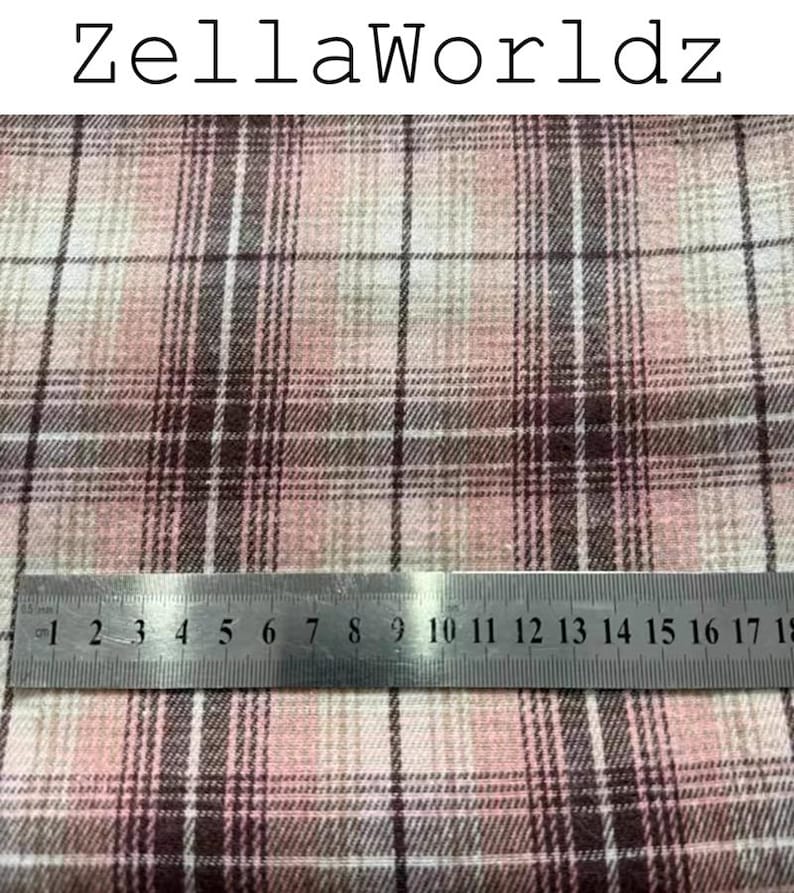 Pu&ograve; includere: Tessuto con motivo a quadri rosa, bianco e marrone scuro con il testo ZellaWorldz in alto. Un righello in metallo &egrave; posizionato orizzontalmente sul tessuto, mostrando le misure in centimetri fino a 18 cm come riferimento di scala.