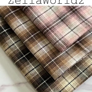Pu&ograve; includere: Tre pezzi di tessuto piegati con un motivo a quadri e il testo ZellaWorldz in alto. Gli strati di tessuto mostrano una tavolozza di colori rosa tenue, varie tonalit&agrave; di marrone, beige e bianco, disposti in una griglia di linee incrociate.