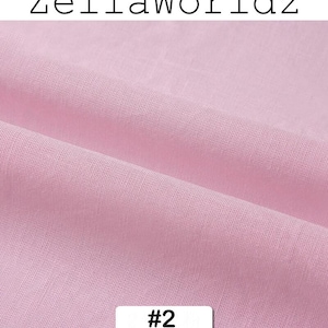Peut inclure: Gros plan sur un tissu rose clair avec une texture visible et des plis. Le tissu porte le texte "ZellaWorldz" en haut et le num&eacute;ro "#2" dans un rectangle blanc en bas. Le tissu semble &ecirc;tre doux.