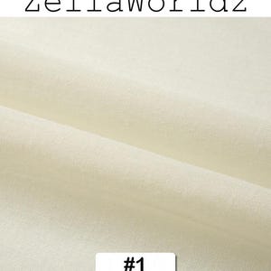 Peut inclure: Gros plan sur un tissu cr&egrave;me avec une texture visible et des plis. Le texte "ZellaWorldz" est en haut, et une &eacute;tiquette avec le num&eacute;ro "#1" est en bas. Le tissu semble &ecirc;tre une mati&egrave;re naturelle.