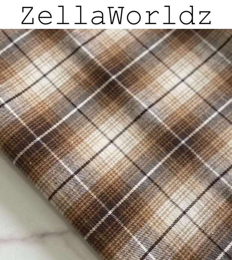 Pu&ograve; includere: Un pezzo di tessuto con un motivo a quadri marrone, beige e bianco con linee che si intersecano. Il testo ZellaWorldz &egrave; stampato in nero nella parte superiore dell'immagine. Il tessuto ha una trama tessuta con un design a griglia ripetuto.