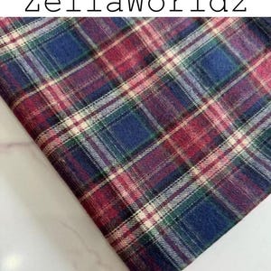 Pu&ograve; includere: Un pezzo di tessuto con un motivo a quadri in tonalit&agrave; rosso scuro, blu navy, verde scuro e sottili linee bianche che si intersecano. Il testo ZellaWorldz &egrave; stampato in nero nella parte superiore dell'immagine, che mostra un tessuto piegato.