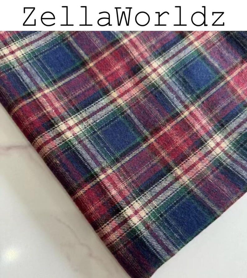 Pu&ograve; includere: Un pezzo di tessuto con un motivo a quadri in tonalit&agrave; rosso scuro, blu navy, verde scuro e sottili linee bianche che si intersecano. Il testo ZellaWorldz &egrave; stampato in nero nella parte superiore dell'immagine, che mostra un tessuto piegato.
