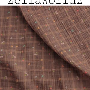 Può includere: Tessuto marrone con un motivo a quadri e piccoli disegni floreali e a farfalla in colori pastello. Il tessuto è piegato, mostrando la sua consistenza e il testo "ZellaWorldz" in alto.