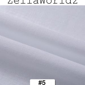 Peut inclure: Gros plan sur un tissu blanc avec une texture et des plis visibles. Le tissu est &eacute;tiquet&eacute; avec le texte "ZellaWorldz" en haut et le num&eacute;ro "#5" dans un rectangle blanc en bas. Le tissu semble &ecirc;tre un mat&eacute;riau l&eacute;ger et respirant.