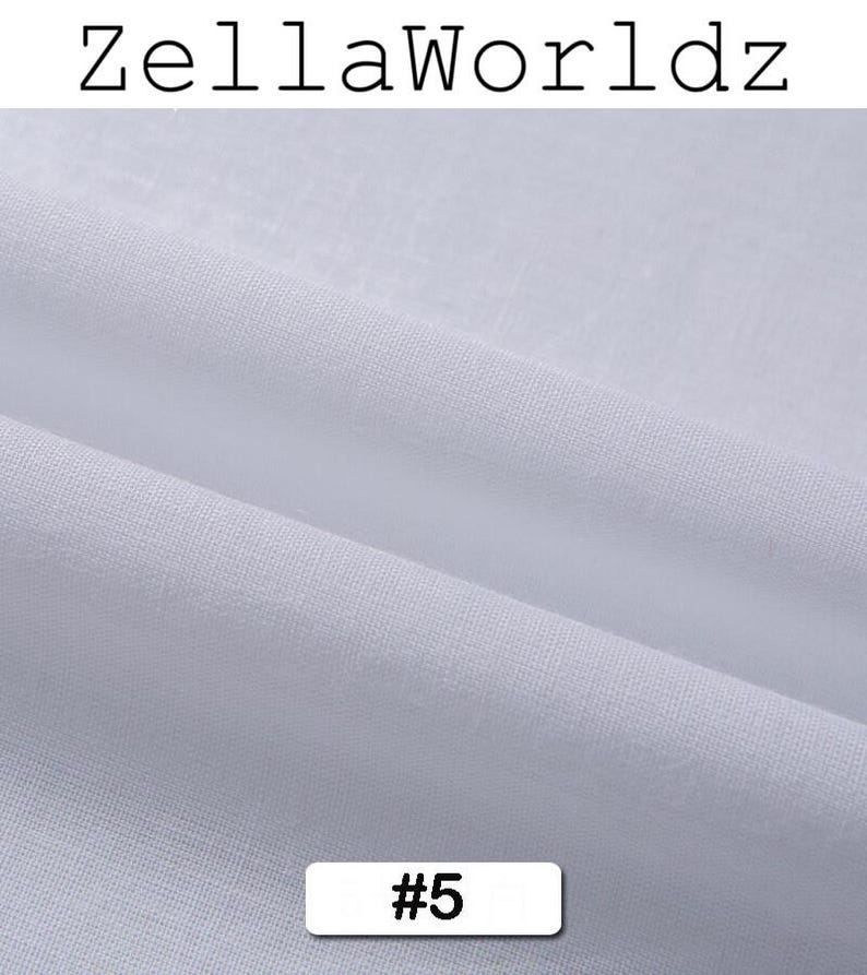 Peut inclure: Gros plan sur un tissu blanc avec une texture et des plis visibles. Le tissu est &eacute;tiquet&eacute; avec le texte "ZellaWorldz" en haut et le num&eacute;ro "#5" dans un rectangle blanc en bas. Le tissu semble &ecirc;tre un mat&eacute;riau l&eacute;ger et respirant.