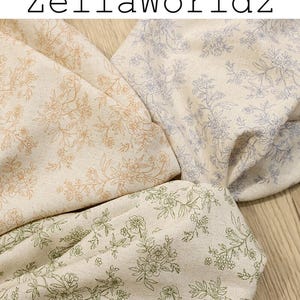 May include: Fabric swatches with floral patterns in beige, green, and lavender. The fabric has a linen-like texture, with the text "ZellaWorldz" at the top. The floral designs are in complementary colors, creating a soft, natural aesthetic.
