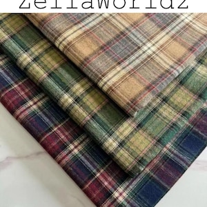 Pu&ograve; includere: Tre strati piegati di tessuto a quadri con il testo ZellaWorldz in alto. Lo strato superiore &egrave; color marrone chiaro, quello centrale &egrave; verde e quello inferiore &egrave; un mix di blu scuro, rosso e verde. Ogni strato mostra un classico motivo a linee.
